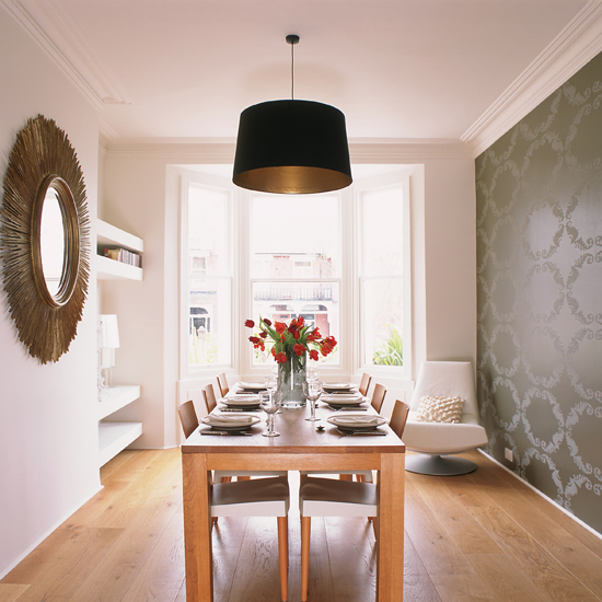 Narrow dining area with wooden table, sunburst mirror and metallic print statement wallpaper