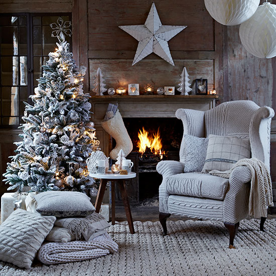 Country Christmas living room with wood panelled wall, fireplace, grey woven rug, cable-knit covered wing chair and Christmas tree
