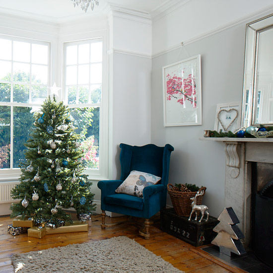 Country Christmas living room with white walls, wood flooring, marble mantlepiece, blue velvet chair and Christmas tree
