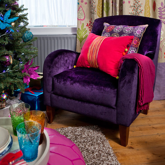 Country Christmas living room with wood flooring, purple velvet chair, bright pink cushion, pink footstool and Christmas tree